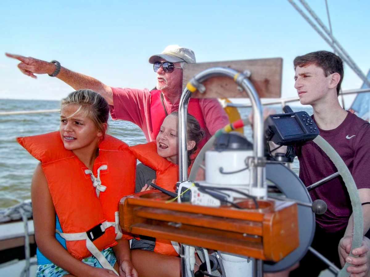 Three children sailing a boat with a captain providing instruction
