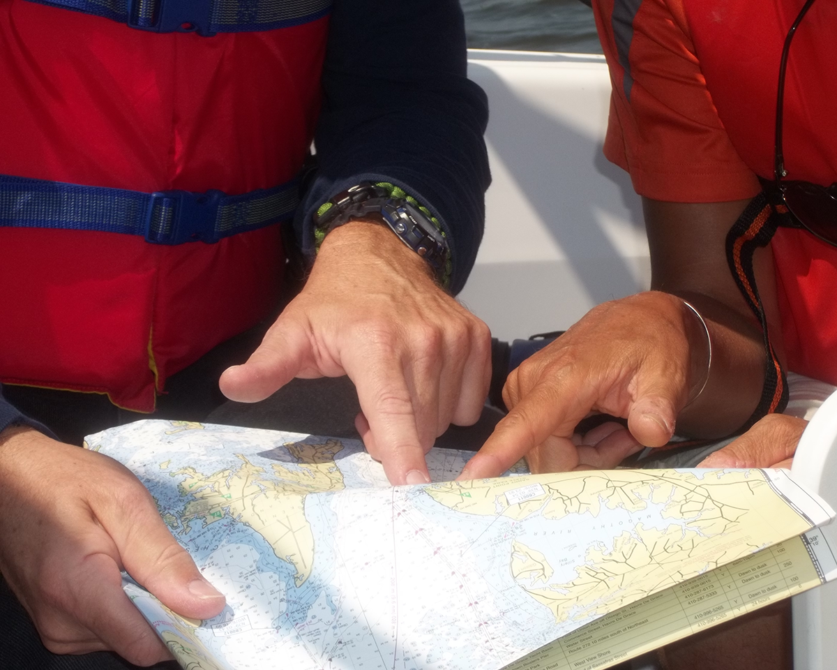 Two sailors pointing to a location on a nautical chart