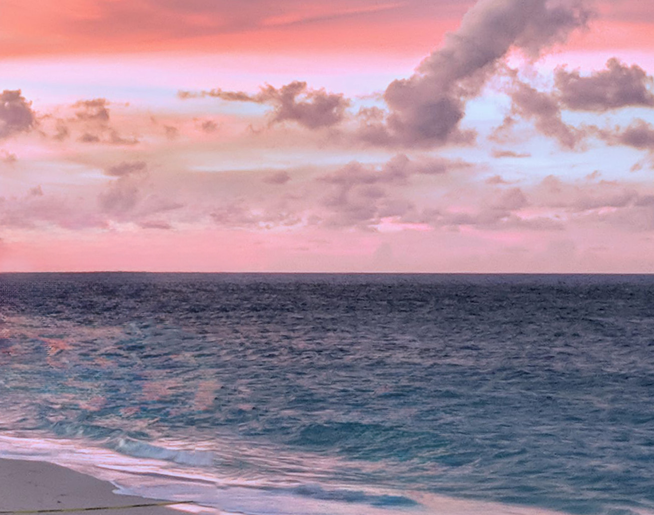 A sunset over the water with a pink sky and puffy clouds